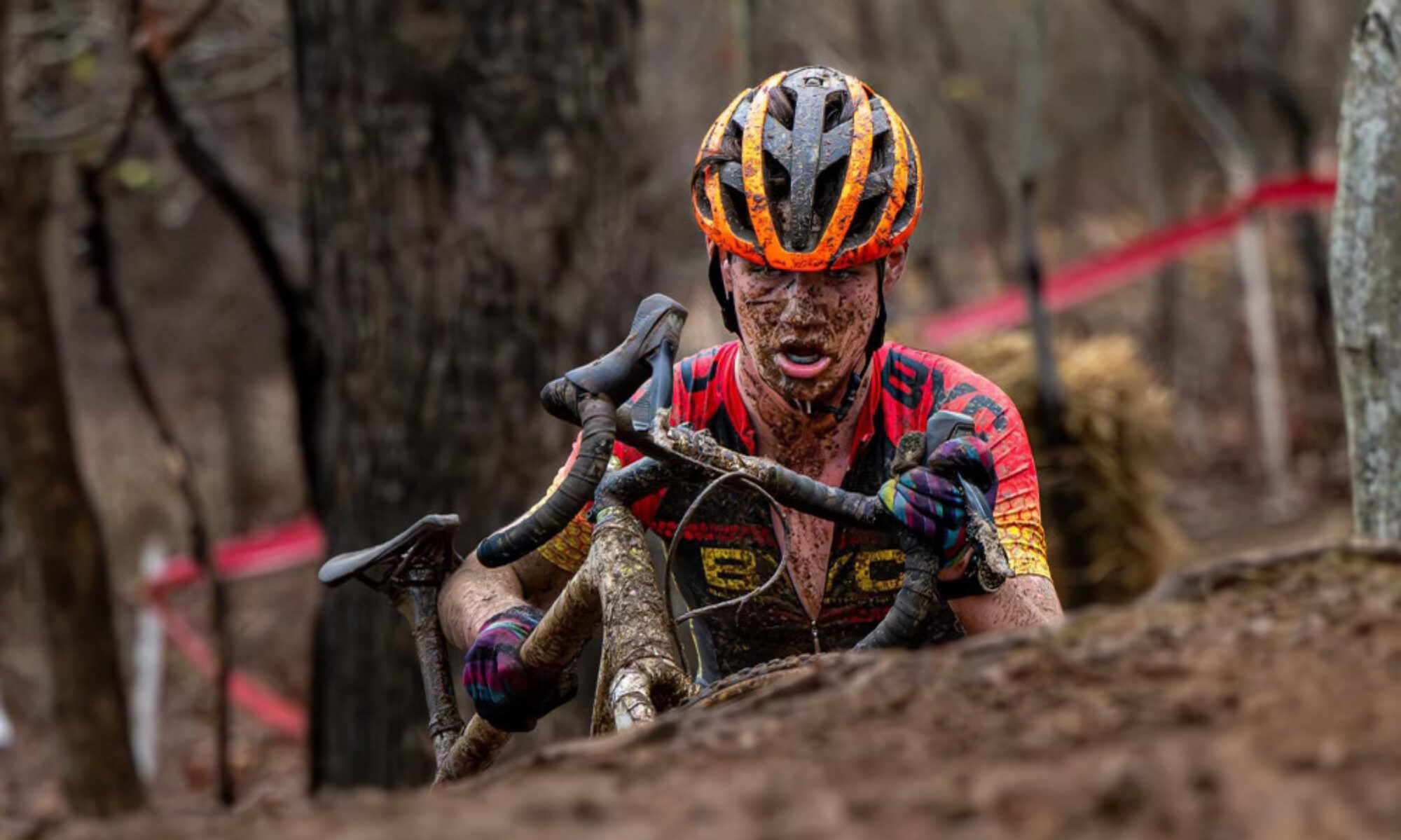 Photo of a racer covered in mud holding a bike